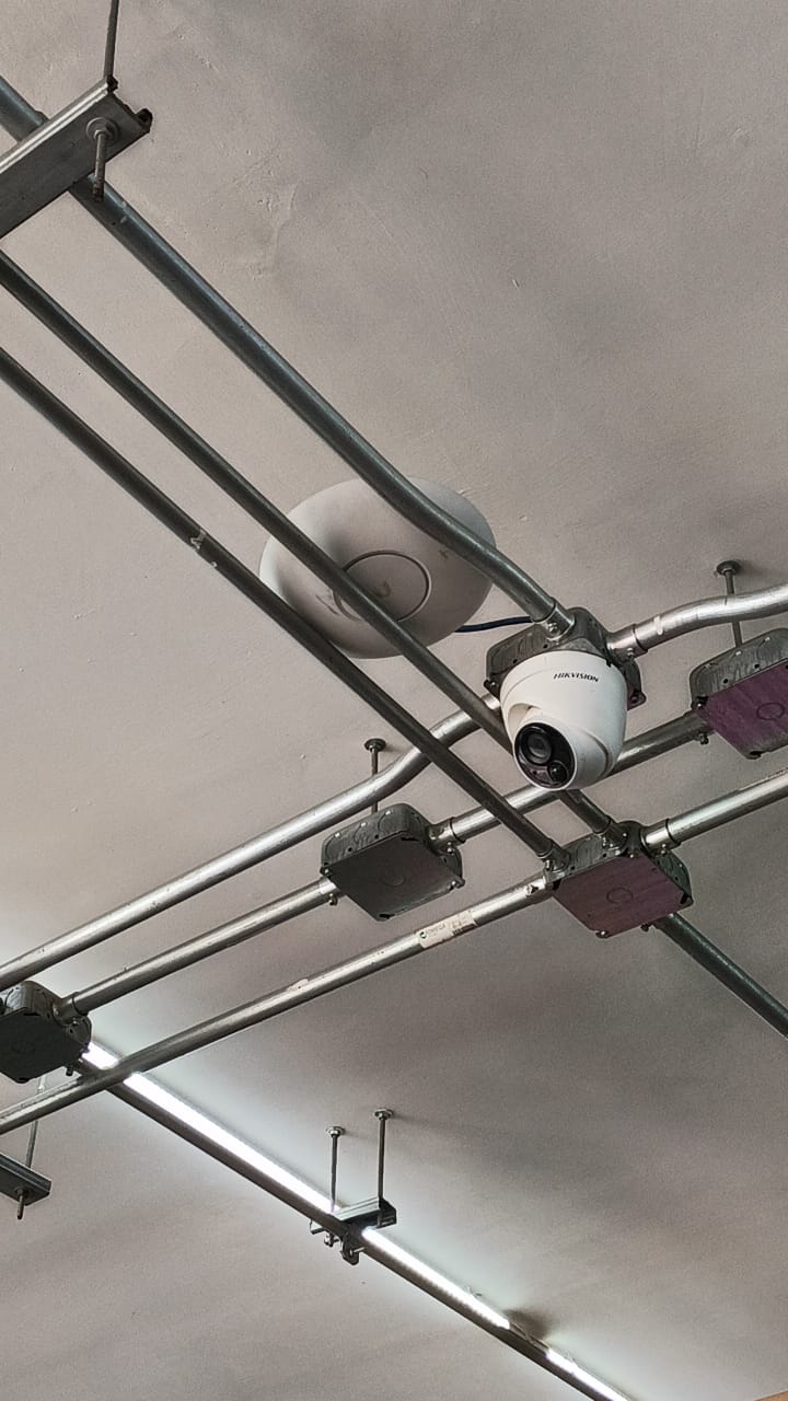 Cámara de vigilancia y punto de acceso instalados junto a tubería en el techo